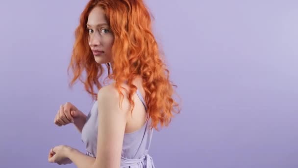 Просмотр видео рыжеволосой женщины, указывающей указательным пальцем на пространство для копирования на спине, смотрящей в камеру, на фиолетовом фоне студии. — стоковое видео