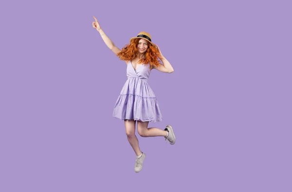 Foto completa de uma menina ruiva engraçada alegre no verão vestido curto com um chapéu de palha pulando e apontando para cima com um dedo. — Fotografia de Stock