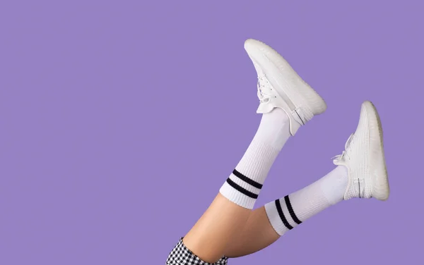 Zugeschnittenes Foto von jungen Schulmädchenbeinen, die mit weißen Socken und Turnschuhen auf lila Hintergrund Schritt halten, Schuluniform-Konzept. — Stockfoto