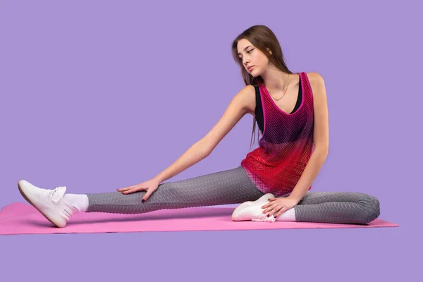 Erős nő test fitness edző, hogy erősítse gyakorlatok jóga szőnyeg öltözött sportruházat lila háttér. — Stock Fotó