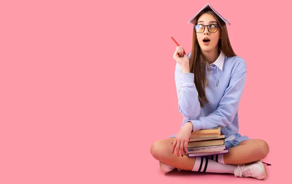 Foto de incrível jovem e bela menina da escola sentado isolado sobre fundo de parede rosa, olhando para o lado e mostrando copyspace apontando, colocação de produto. — Fotografia de Stock
