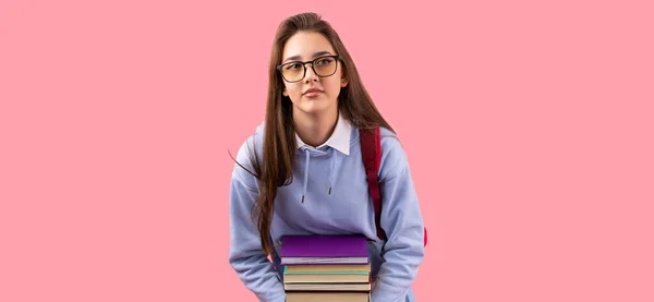 Крупним планом фото школярки красива дівчина в окулярах з рюкзаком в шкільній формі, що тримає величезний стек книг . — стокове фото