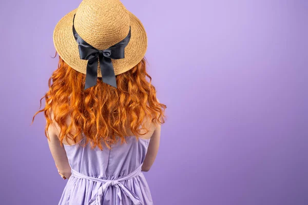 Imagem da mulher ruiva de volta em sundress usando um chapéu de palha com uma fita posando no fundo roxo e espaço de cópia. — Fotografia de Stock