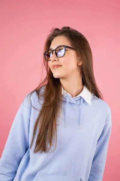 Jovem estudante universitária alegre com cabelo longo loiro vestindo óculos olhando para o fundo rosa isolado. — Fotografia de Stock
