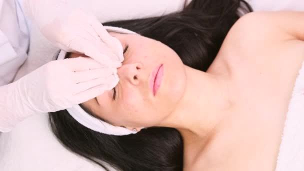 Eldivenli kozmetik uzmanı güzellik kliniğindeki kadının yüzündeki kozmetik maskeyi çıkarmak için iki pamuk pedi kullanıyor.. — Stok video