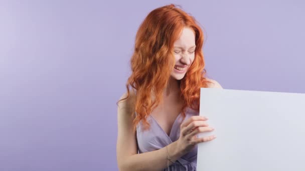 Rozczarowana ruda stylowa dziewczyna pokazuje puste białe miejsce do reklamy, młoda kobieta na fioletowym tle studio. — Wideo stockowe