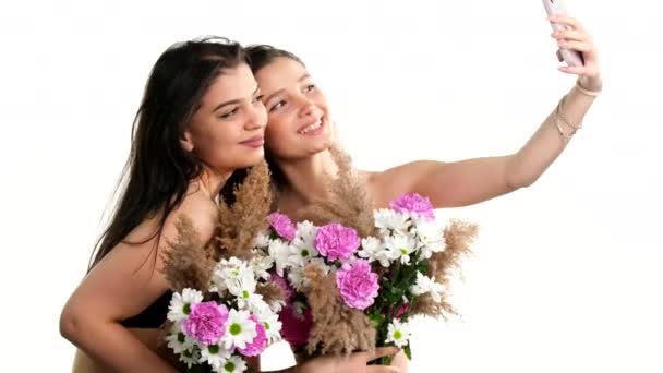 Két szerelmes lány virágcsokrot tart a mellén, és érzéki fotót készít mobiltelefonnal.. — Stock videók