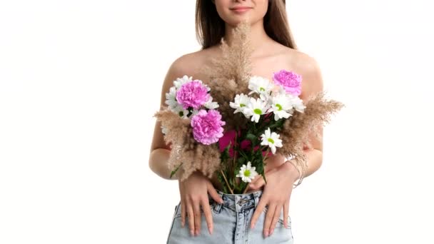 Mooie glimlachende jonge dame die haar borst bedekken met veld boeket bloemen poseren over witte achtergrond en kopieer ruimte. — Stockvideo