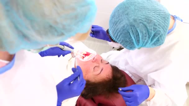 Стоматолог с ассистентом, работающим с женскими зубами у пациентки, используя стоматологические инструменты в стоматологической клинике. — стоковое видео