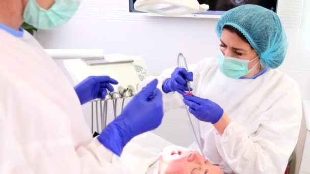 Дантист работает в современной стоматологической клинике с ассистентом, помогающим пациентке с зубами. — стоковое видео