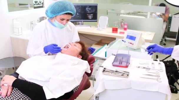 Concentrado tenso bonito mulher sênior deitado na cadeira dentistas e segurando a boca aberta enquanto dentista examinando sua saúde dental. — Vídeo de Stock