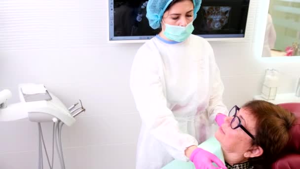 Mulher dentista vestindo uniforme e máscara médica com luvas preparando um paciente para o procedimento e explicando como ele vai passar. — Vídeo de Stock