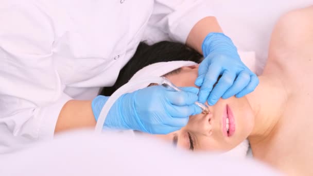Profesionální kosmetolog provádějící omlazovací proceduru s elektrickým mikrodermabrazionním vakuovým masážním přístrojem na ženském nose. — Stock video