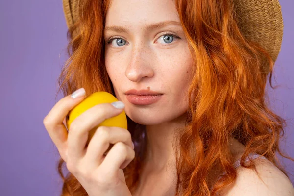 Портрет красивої молодої рудої жінки з блакитними очима і веснянками в солом'яному капелюсі, що тримає яблуко закритим до її обличчя . — стокове фото