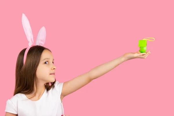 Фотографія маленької красивої дівчинки, яка дивиться вбік, носить вуха кролика на голові, тримаючи подарунок у простягнутій руці . — стокове фото