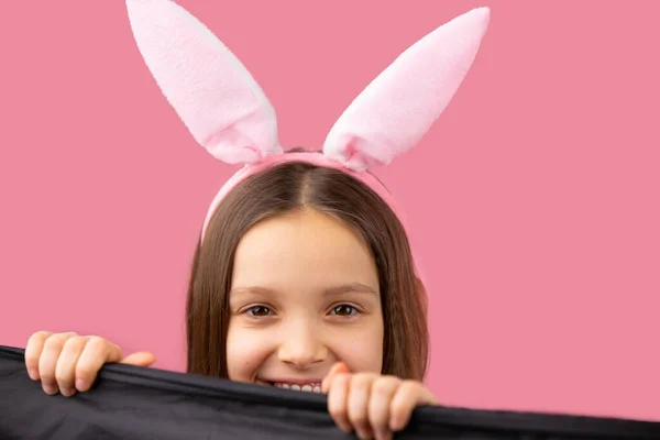 Обрізана фотографія красивої усміхненої дівчини з світлим волоссям у вухах кролика на голові, дивлячись на камеру, що позує на рожевому фоні . — стокове фото