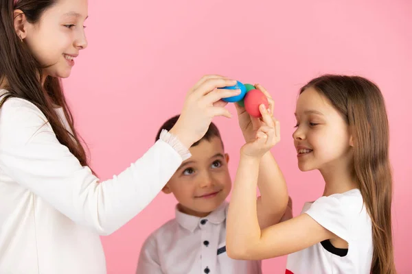 Familj av tre barn som håller händerna upp med målade ägg och hålla ihop dem på rosa bakgrund, påsk koncept. — Stockfoto