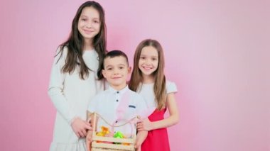 Üç çocuklu aile bir arada gülümsüyor ve küçük çocuk elinde boya dolu yumurta ve hediyelerle Paskalya tatili için sepet tutuyor..
