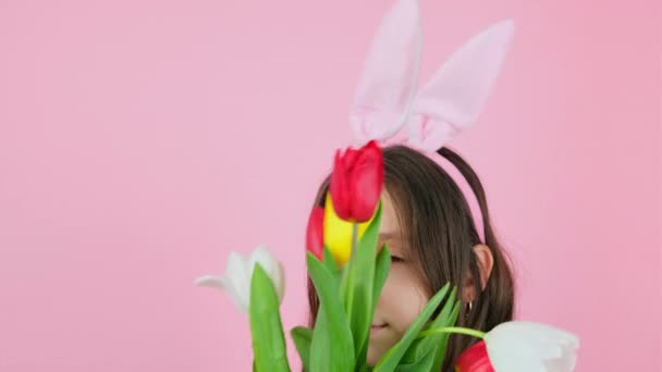 Croppde vidéo d'une fille drôle portant des oreilles de lapin cachant visage avec des fleurs, puis les enlève du visage sur fond rose. — Video