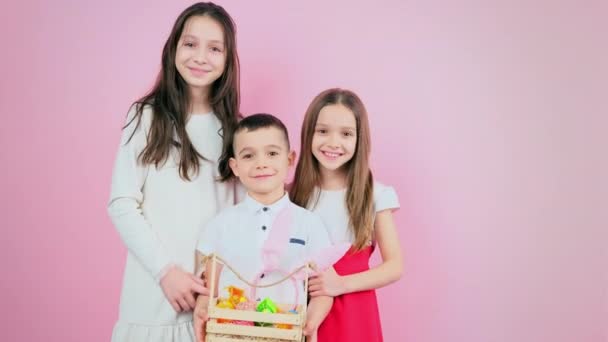Famiglia di tre bambini in piedi insieme sorridente e bambino che tiene cesto con uova dipinte e regali per le vacanze di Pasqua. — Video Stock