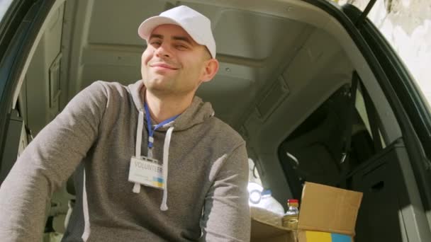 Přátelský usmívající se upřímný kavkazský dobrovolník s darem pro Ukrajinu. Spokojený pohledný muž držící dárcovskou krabici pro uprchlíky na ulici. — Stock video