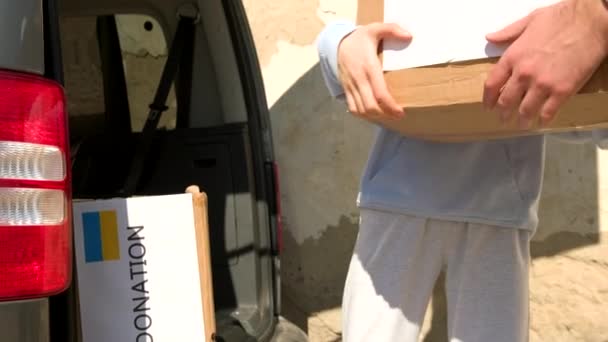 Zwei freiwillige Männer und eine junge Frau werden aus den Kartons mit gespendeten Lebensmitteln und Getränken für die Flüchtlinge aus der Ukraine entladen. — Stockvideo
