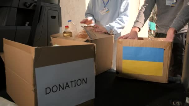 Två frivilliga förpackningar lådor med mat, dryck och medicinska masker för flyktingar från Ukraina, humanitär hjälp koncept. — Stockvideo