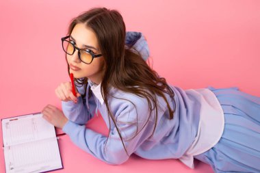 Okul üniformalı, gözlüklü, yerde yatan ve kameraya, üniversite konseptine bakan harika bir genç kızın en iyi görüntüsü..