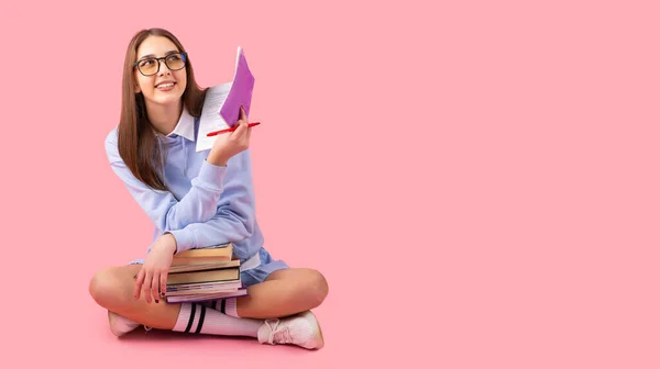 Menina da escola muito loira pensativo olhando para cima com um sorriso sentado no chão com pernas cruzadas segurando livros e um diário com uma caneta, conceito de universidade do ensino médio. — Fotografia de Stock