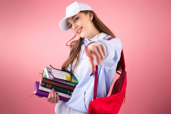 Jovem sorrindo feliz com mochila segura livros e mochila com um boné na cabeça isolada estendeu a mão para a câmera. — Fotografia de Stock