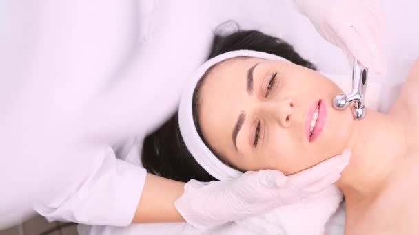 Foto ritagliata di cosmetologo in guanti utilizzando cosmetici rullo a forma di Y per il massaggio lifting facciale a una donna in una clinica di bellezza, concetto di cura della pelle. — Video Stock