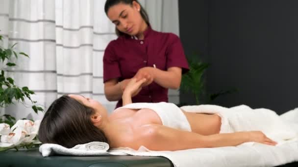Profesjonalny masażysta w mundurze stojący przy stole do masażu i wykonujący zabieg masażu dłoni młodej kobiecie w salonie spa. — Wideo stockowe