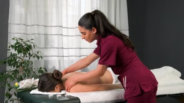 Professionell massör lägga olja på händerna och började göra massage på kvinna klient tillbaka liggande på bordet med ansiktet ner i spa salong. — Stockvideo