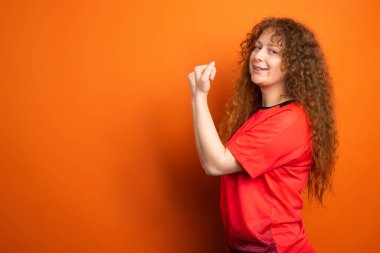 Futbol formalı genç bir kadın en sevdiği futbol takımına yumruk atıyor. Kazanan turuncu stüdyoda tek başına. Yüksek kalite fotoğraf