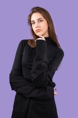 Siyah elbiseli, etkileyici bir görünüşü olan genç ve şık bir iş kızı elini mor arka planda tutuyor..
