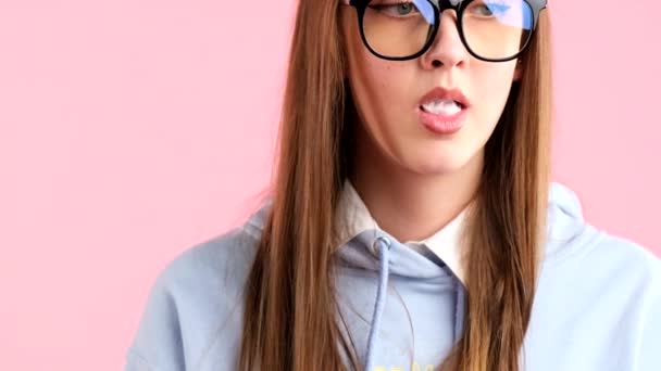 Przycięte wideo ładnej młodej blondynki nastolatki z długimi włosami w okularach, robiącej gumowe bąbelki na różowym tle. — Wideo stockowe