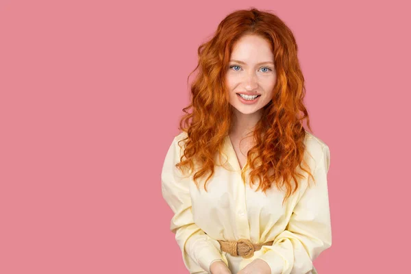 Simpatik kızıl saçlı, mavi gözlü, pembe arka planda mutlu bir yüz ifadesiyle kameraya poz veren genç bir kadın..