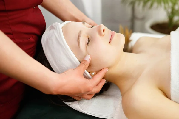 Close up photo of a amazing young woman face with closed eyes undergoing face massage procedure in spa salon, face care concept. — Stock Photo, Image