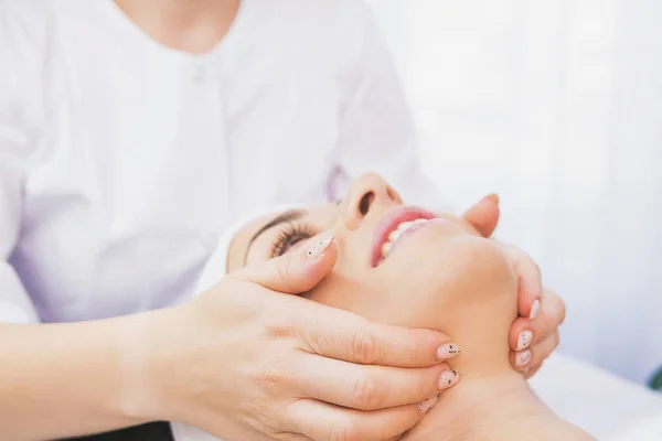 Foto ritagliata di estetista fa una procedura di massaggio facciale per un viso femminile, cliente in una clinica cosmetica, concetto di cura della pelle del viso. — Foto Stock