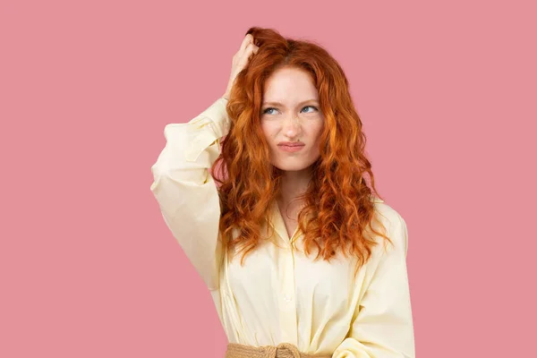 Sarı tunik giymiş düşünceli kızıl saçlı genç bir kadının resmi elini başının üstüne koydu ve pembe arka plana baktı..