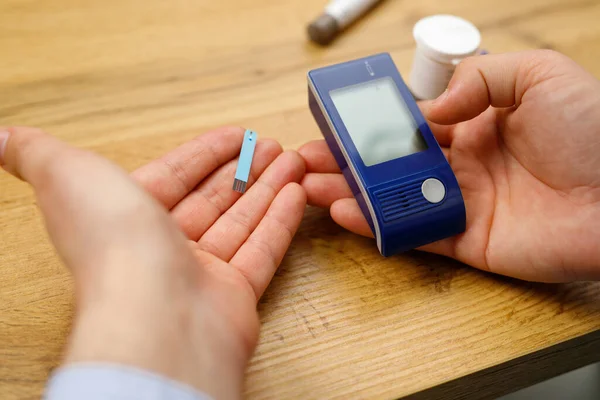 Man hands on the table holding glucometer and stripes for checking blood sugar level, diabetes concept. — Foto de Stock