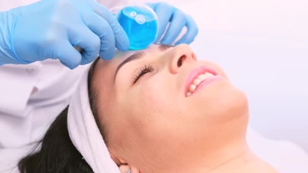 Professional cosmetician in blue gloves doing rejuvenation and relaxing procedure to a woman with facial ball roller massage instrument. — Stock video