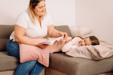 Akşamları küçük kızı için kitap okuyan şefkatli bir anne. Kız uyurken başını yastığa koyuyor..