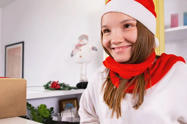 Blonde young woman sitting on her work place in the office in Santa hat and red scarf smiling, holiday concept and copy space. High quality photo
