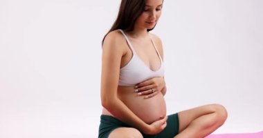Cropped slowmo shot of pregnant woman sitting in lotus pose on yoga mat meditating and stroking her belly. High quality 4k footage