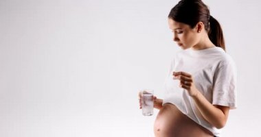 The young mother-to-be in a white t-shirt puts the vitamin in the water and starts drinking. High quality 4k footage