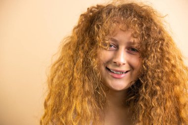 Picture of a funny joyful redhead pretty smiling woman looking at the camera over a golden background, copy space. High quality photo
