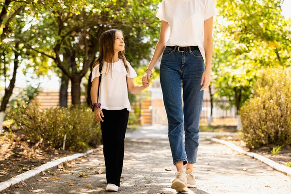 Mother and daughter walk hand in hand on the way to school, the daughter is a little scared and looks at her mother. High quality photo