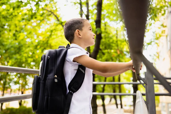 The beautiful student looks towards the school that will teach him, the first day of school. High quality photo