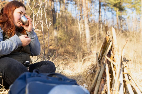 Woman resting in the nature sitting near the bonfire drinking hot tea from a mug on winter day and feeling calm. High quality photo